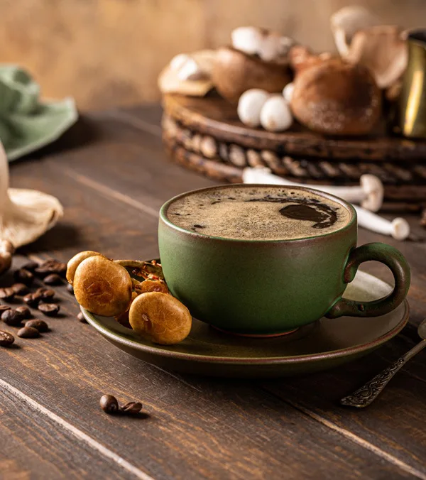 Šalica mushroom coffee kave s gljivama na drvenom stolu uz zrna kave i sušene gljive.